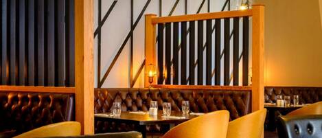 Un interior de restaurante con respaldos de madera, asientos tipo cabina de cuero y lámparas colgantes.