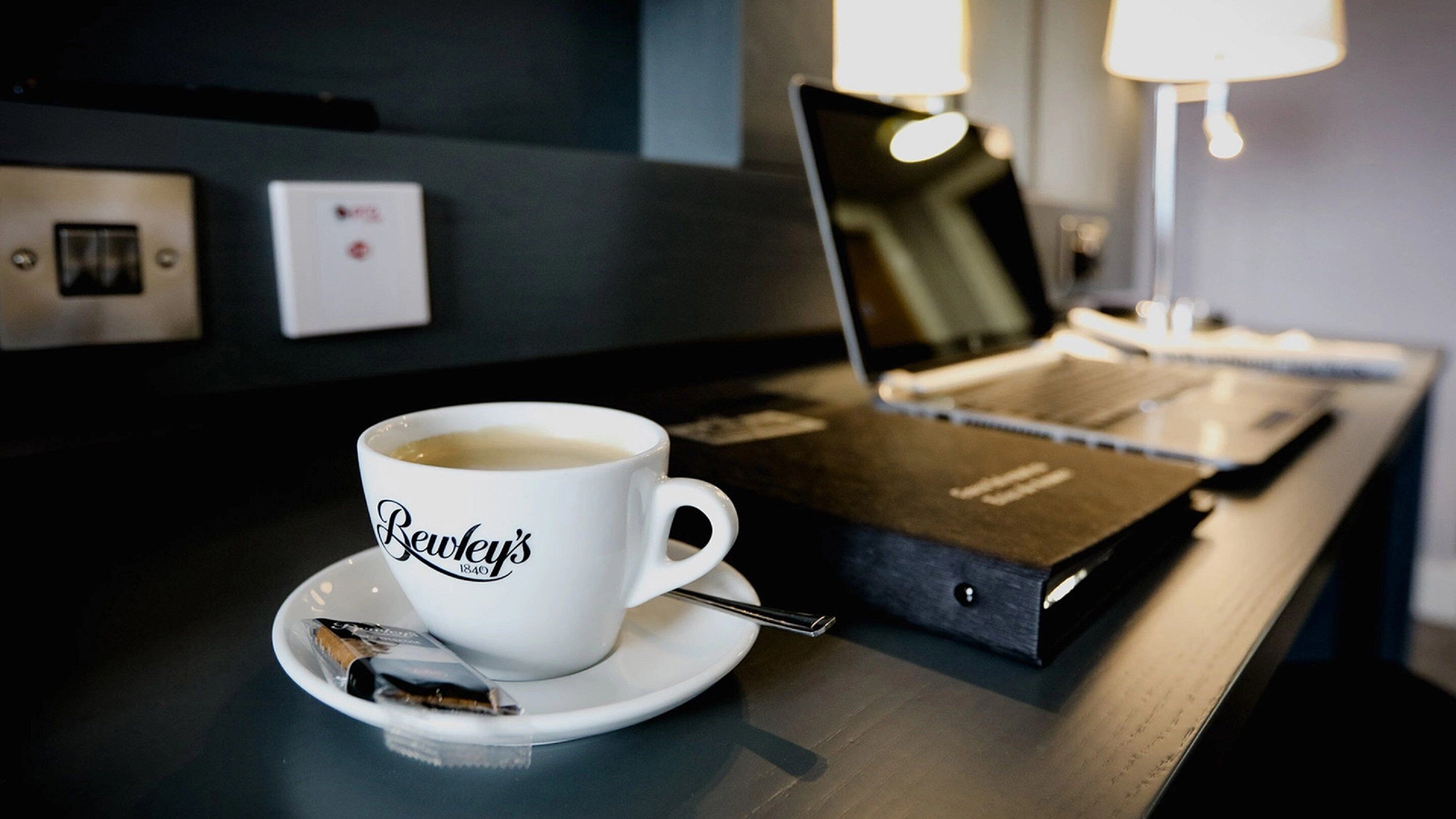 Una taza de café sobre un plato, un paquete de azúcar, una libreta y un bolígrafo en una mesa.
