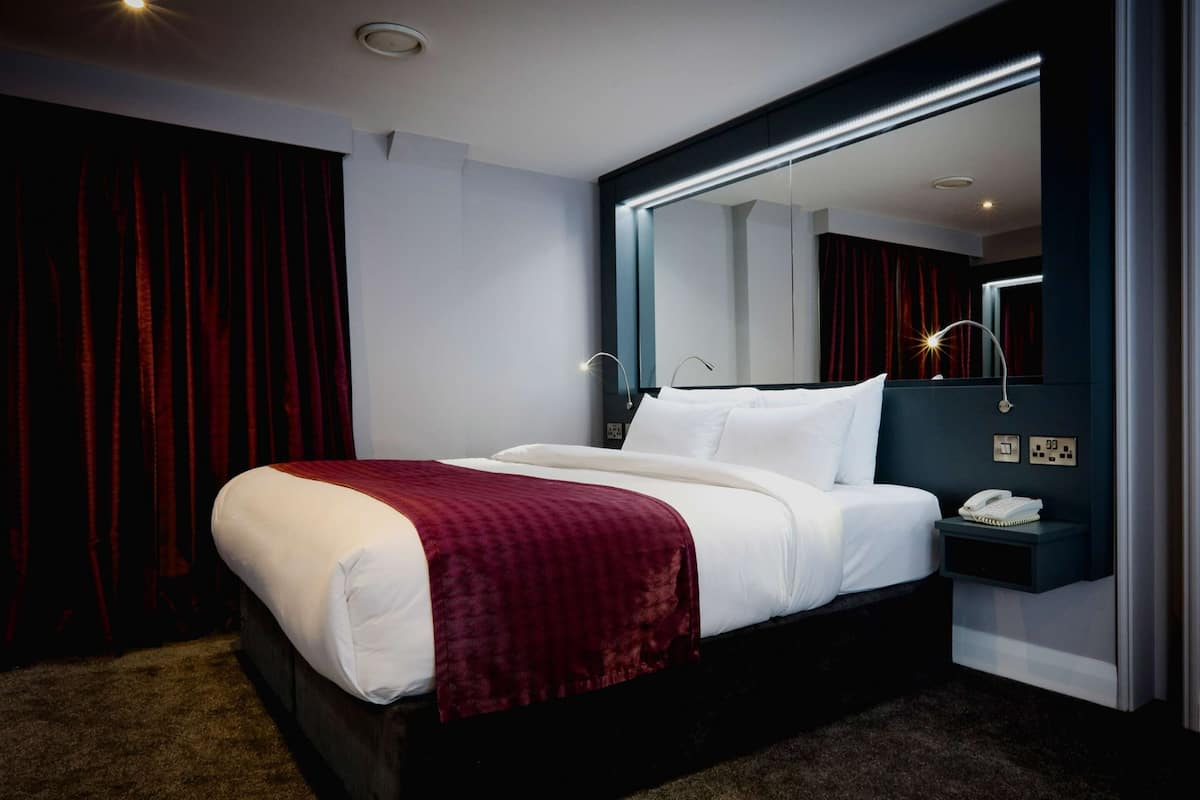 Une chambre d’hôtel moderne avec un grand lit, une table de chevet avec un téléphone et un miroir au-dessus du lit.