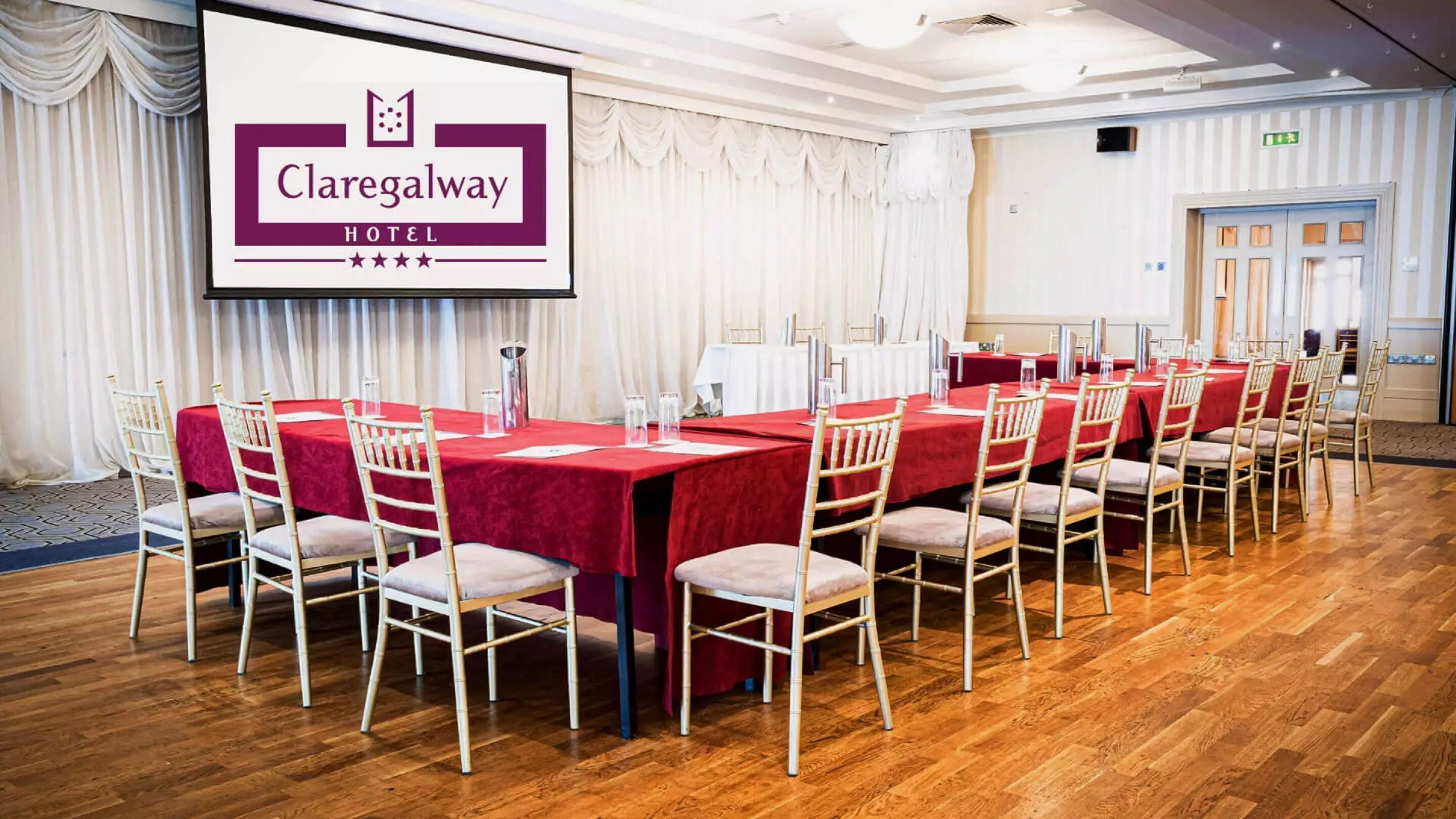 A conference room at Claregalway Hotel with a long table set for meetings, white chairs, and a large screen displaying the hotel name.