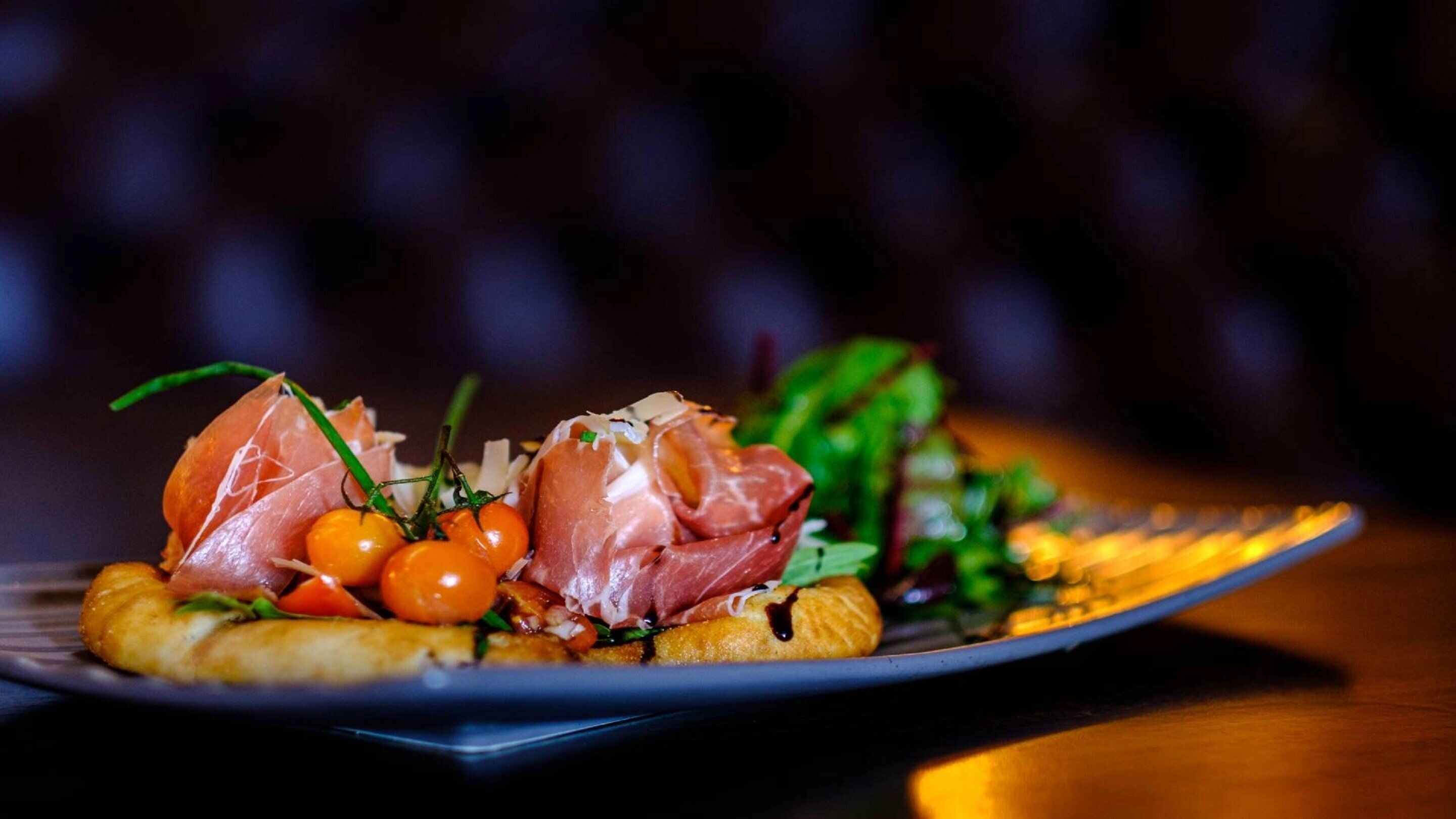 Un plato con un guiso de jamón serrano, tomates cherry y hojas verdes.