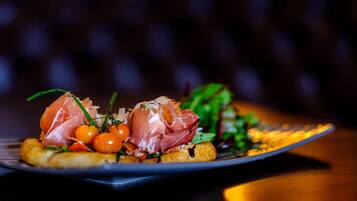 A plate with a dish consisting of prosciutto, cherry tomatoes, and greens.