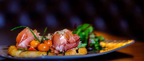 Un plato con un guiso de jamón serrano, tomates cherry y hojas verdes.