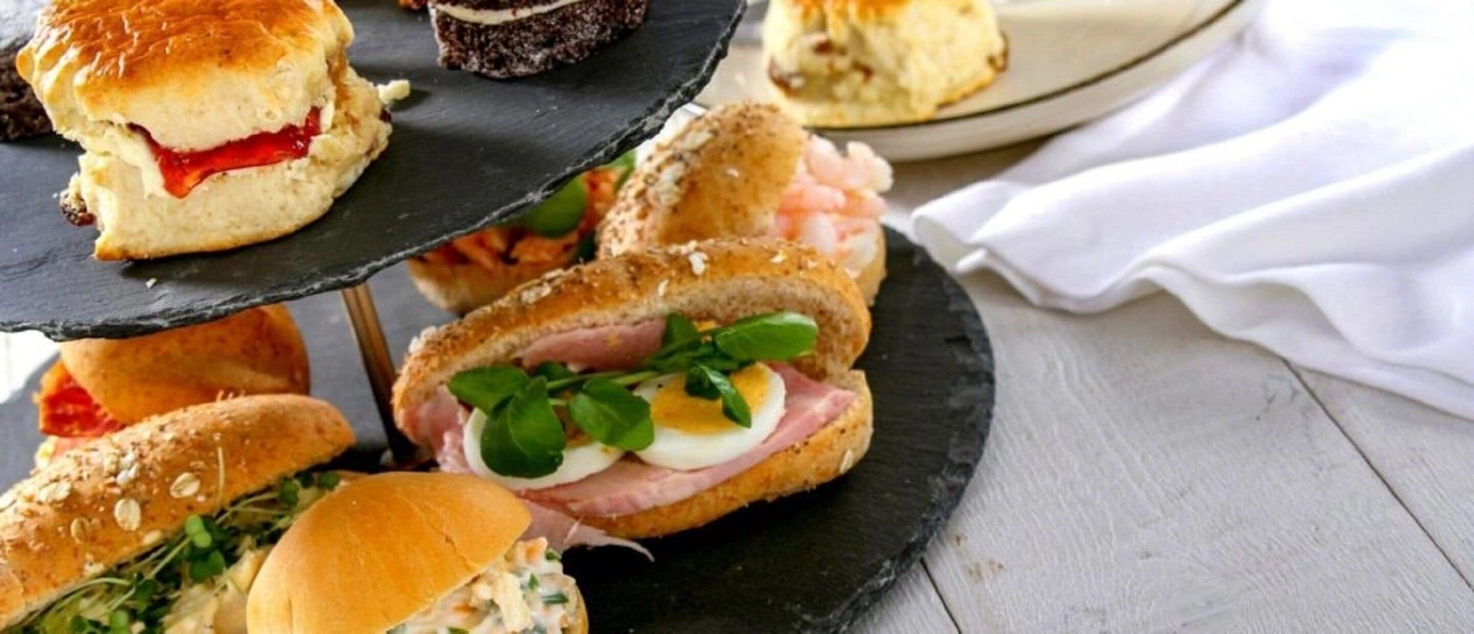 A multi-tiered serving board with various sandwiches and pastries.