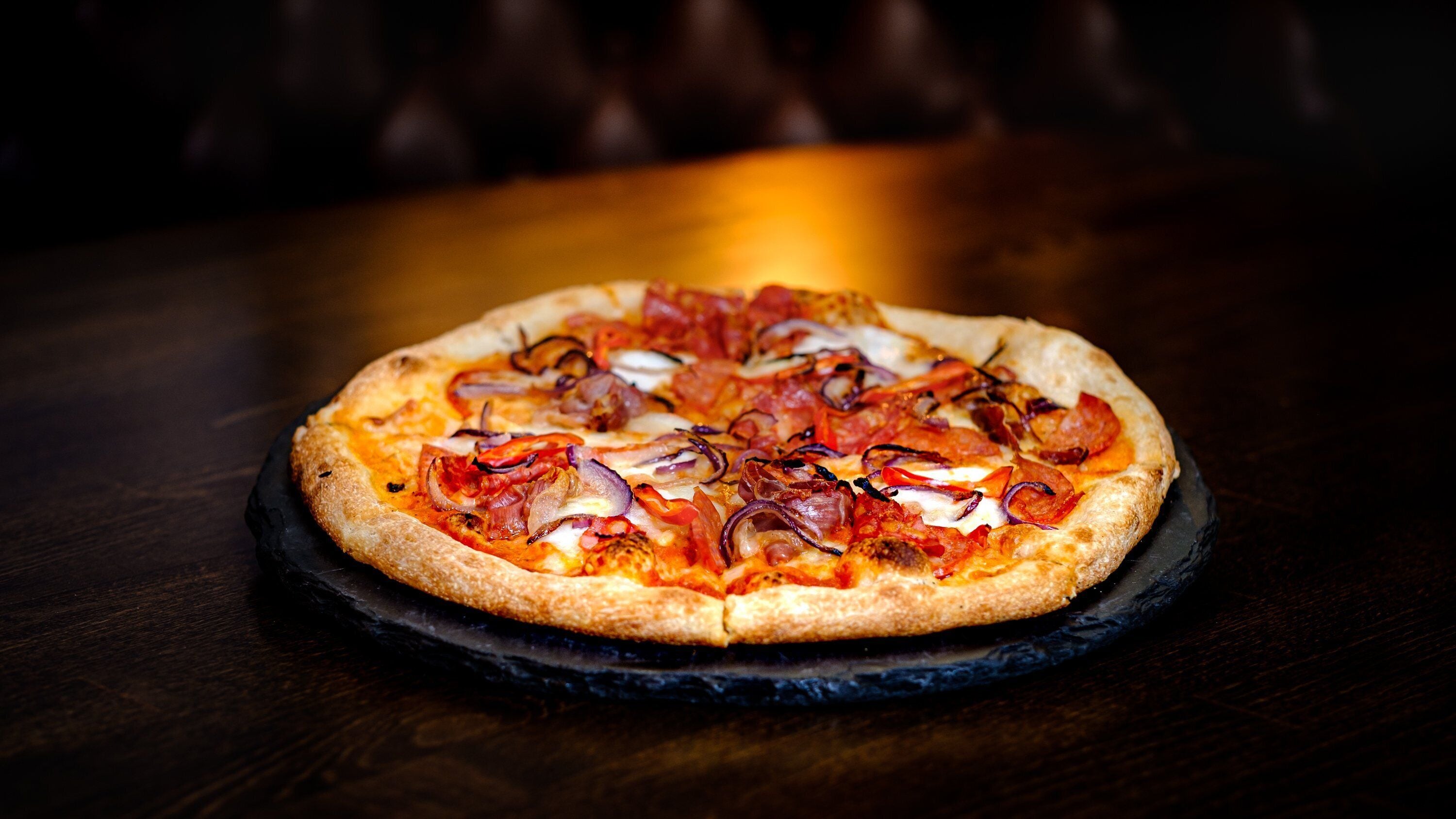 A pizza on a black slate plate on a wooden table.