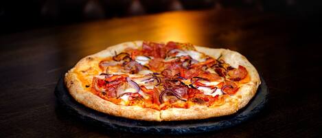 A pizza on a black slate plate on a wooden table.