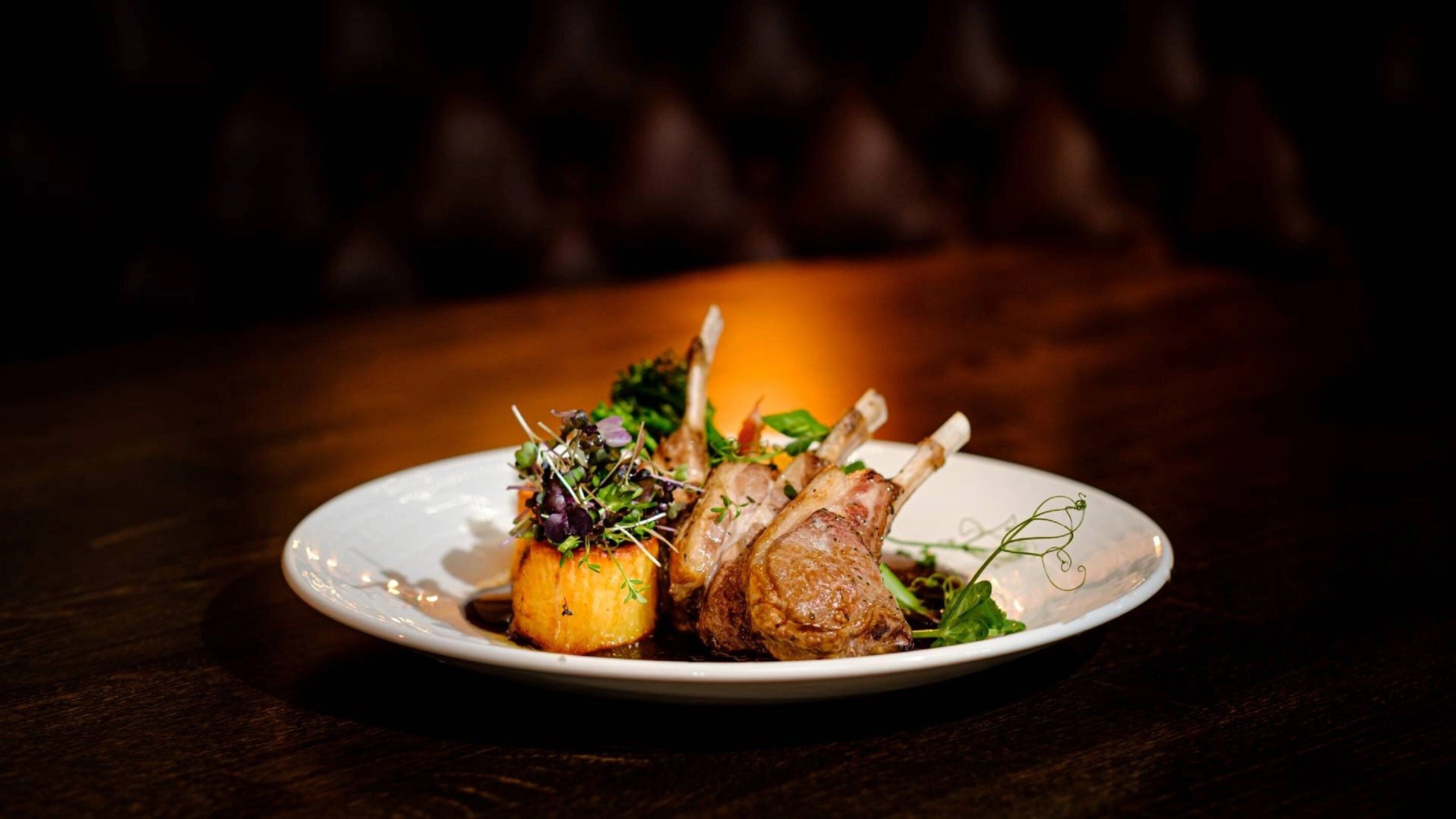 A plate of food with lamb chops and roasted potatoes, garnished with greens, on a white plate.