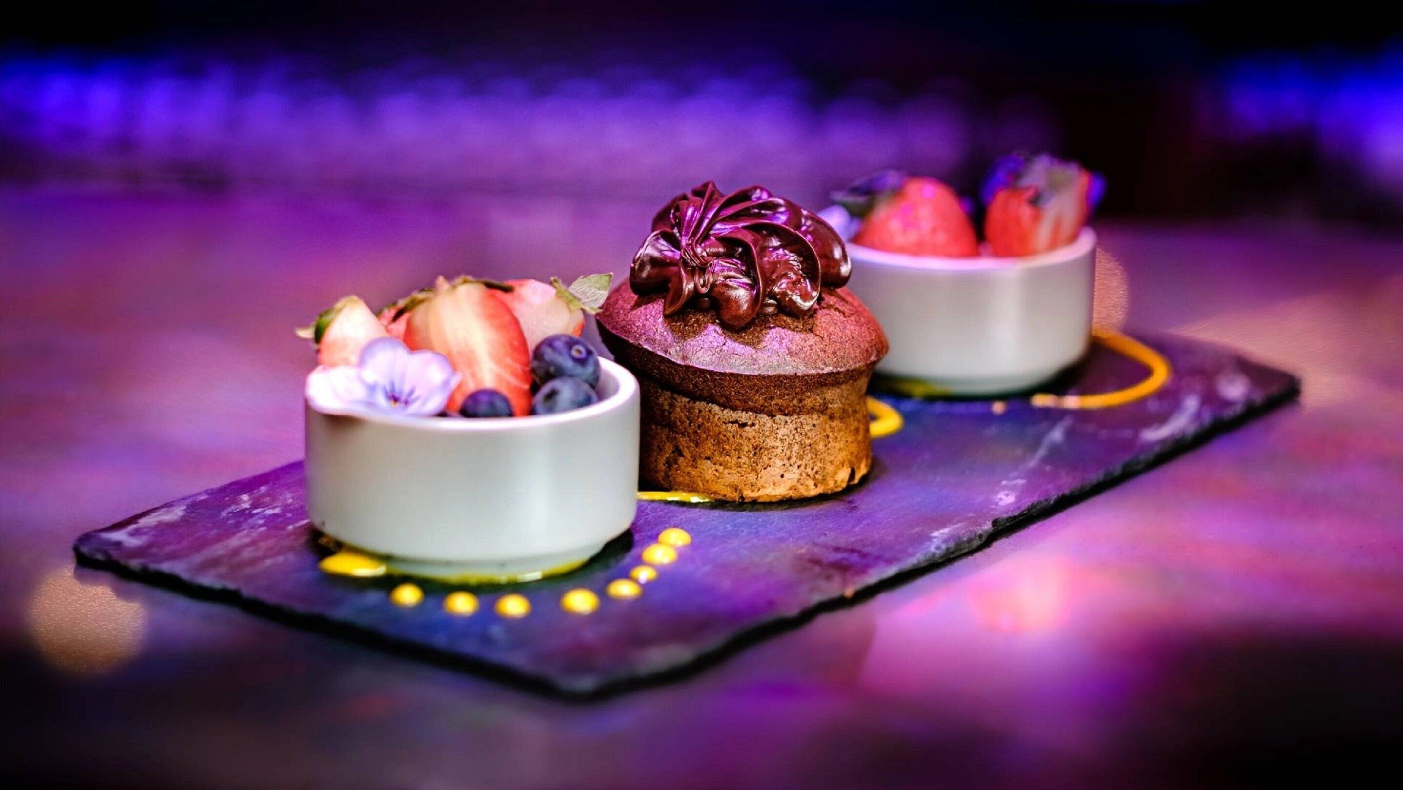Een dessertpresentatie met een taart en schalen vol fruit op een arduin bord.