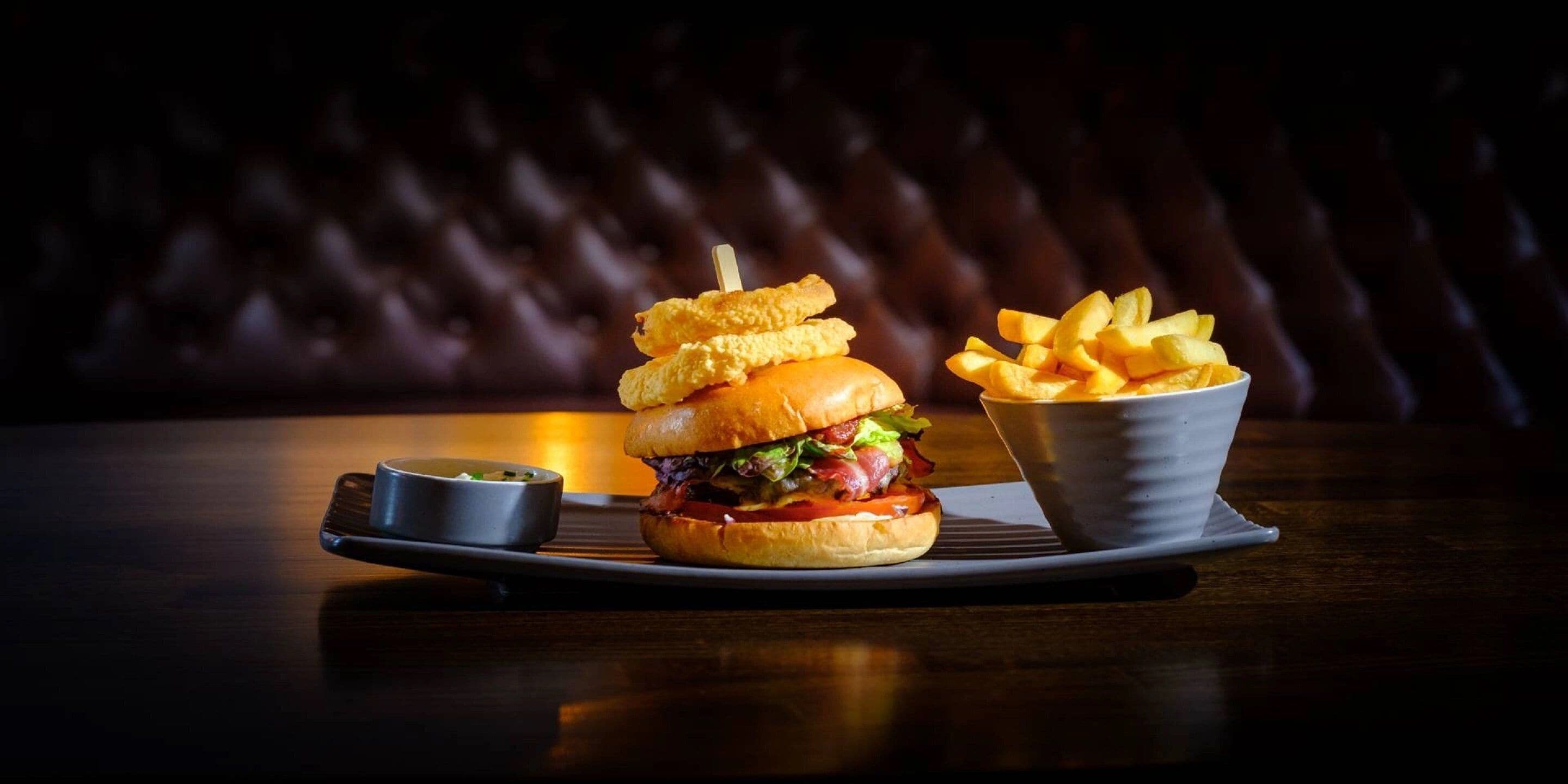 A burger with a side of fries and a small bowl of sauce on a tray.