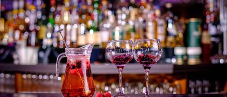 Un bar con un jarro y dos vasos llenos de una bebida roja, frutos rojos y una pajita.