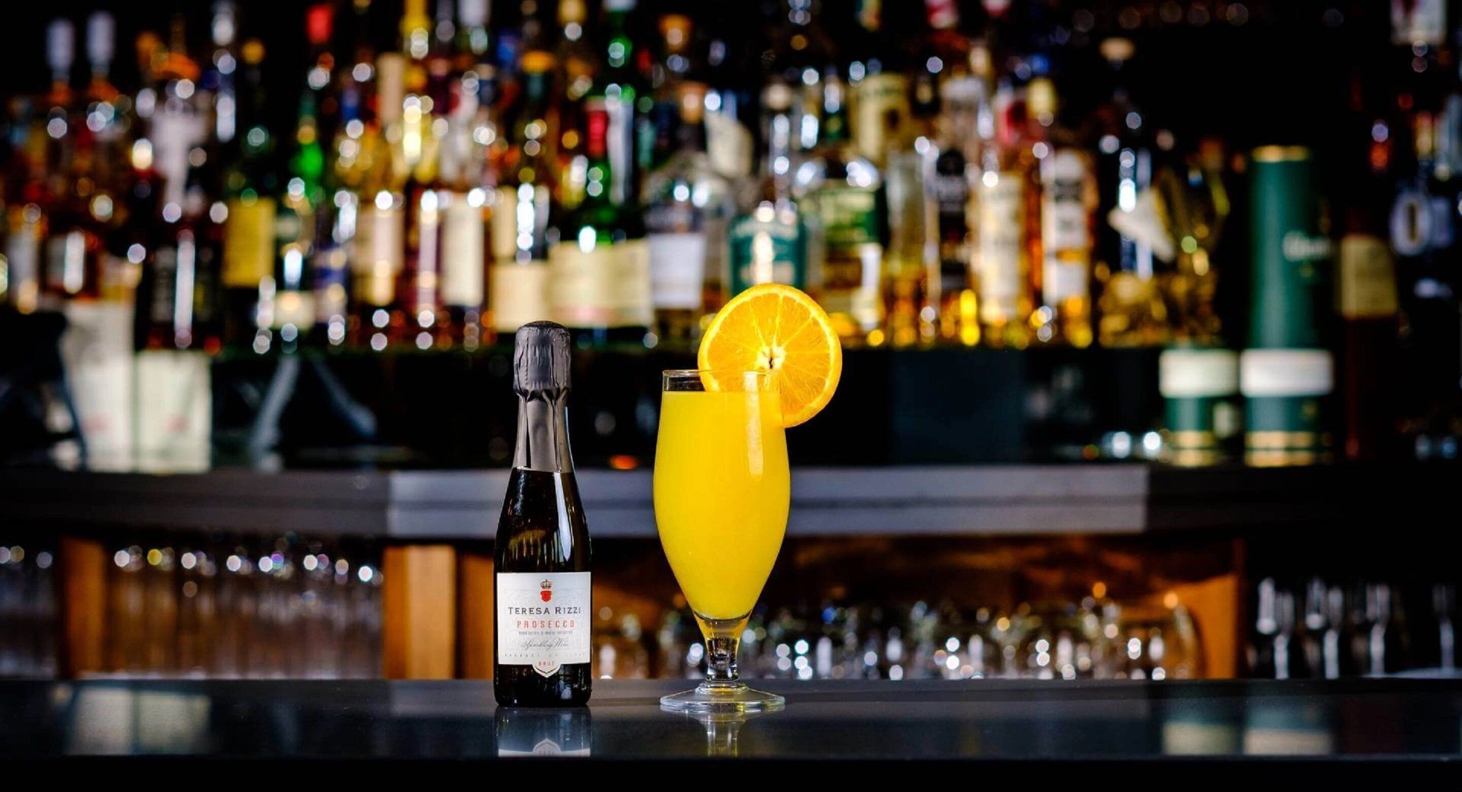 Eine Bar mit einer Flasche Teresa Rizzi Prosecco und einem Glas Orangensaft mit Orangenscheibe.