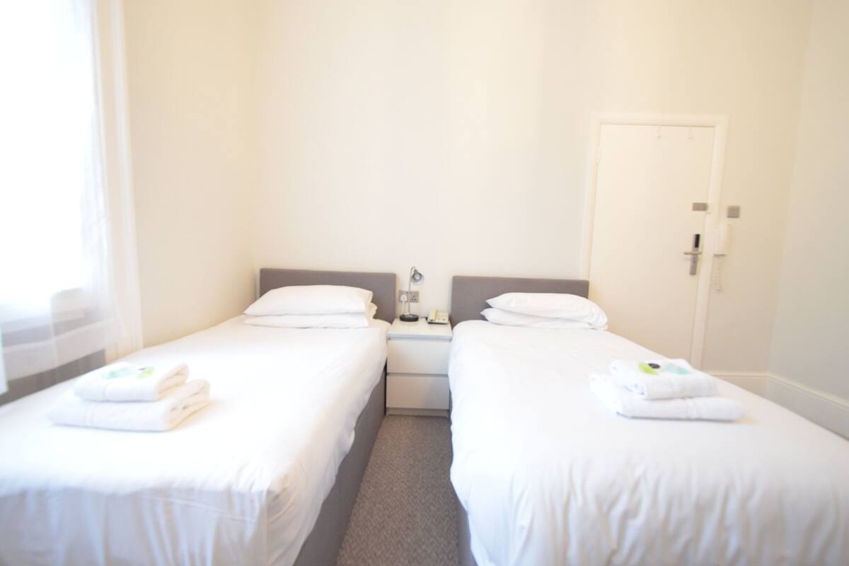 A hotel room with two single beds, a nightstand with a phone, and a door.