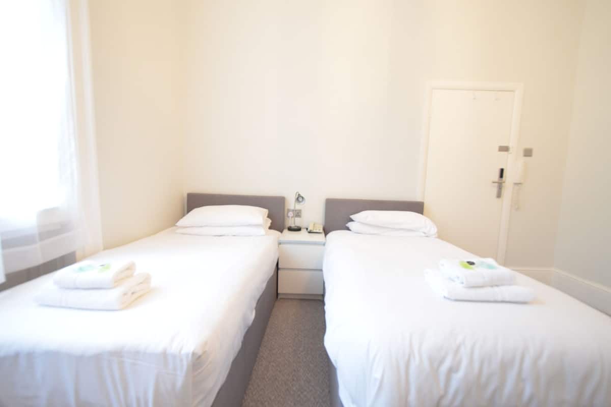 Ein Hotelzimmer mit zwei Einzelbetten, einem Nachttisch mit Telefon und einer Tür.