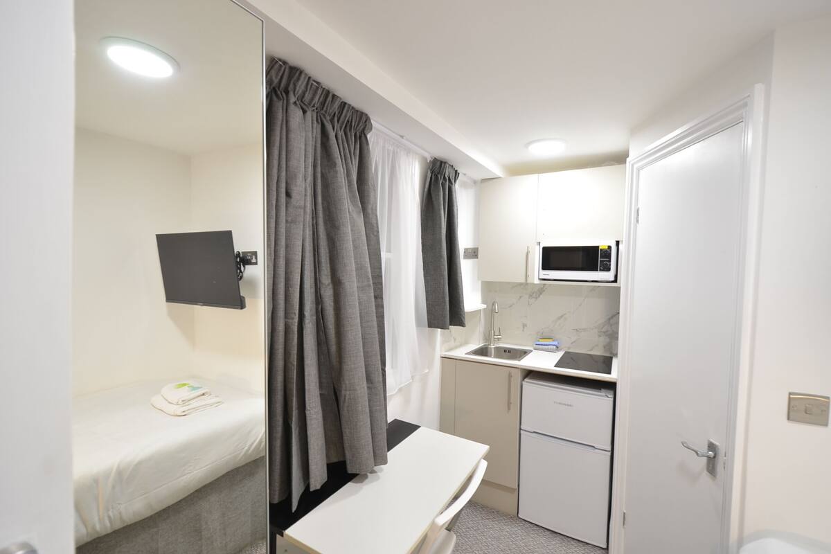 A compact hotel room with a single bed, a small kitchenette, a microwave, and a toilet.