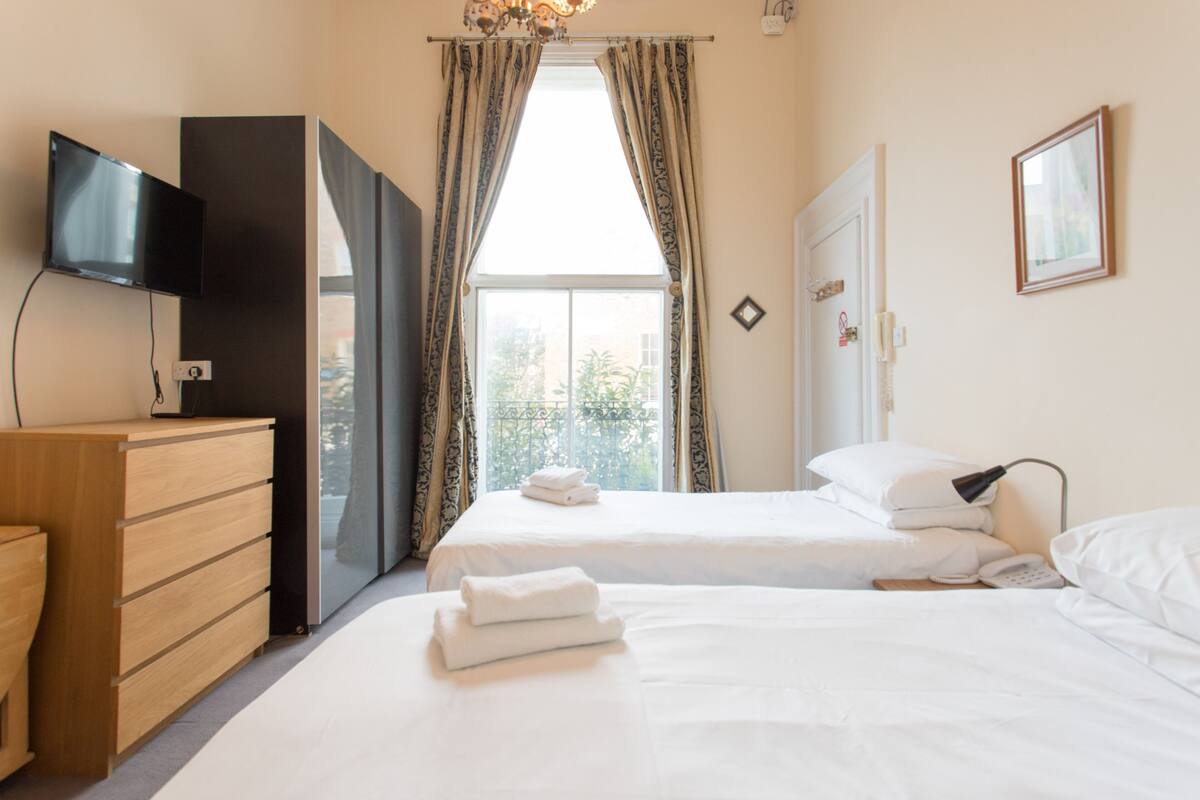 A hotel room with two beds, a TV, a wardrobe, and a window with curtains.