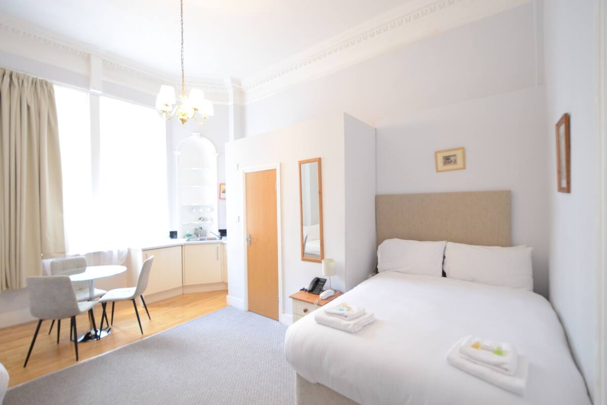 A hotel room with a bed, a desk, a chair, a small table, and a mirror.