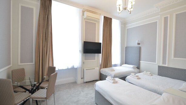 A hotel room with a glass table, two beds, a TV, and a chandelier. - Amber Residence Hotel (London)