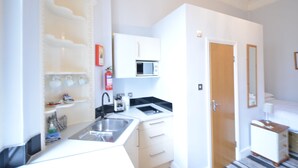 A compact kitchen with white cabinets, a microwave, and a sink. - Amber Residence Hotel (London)