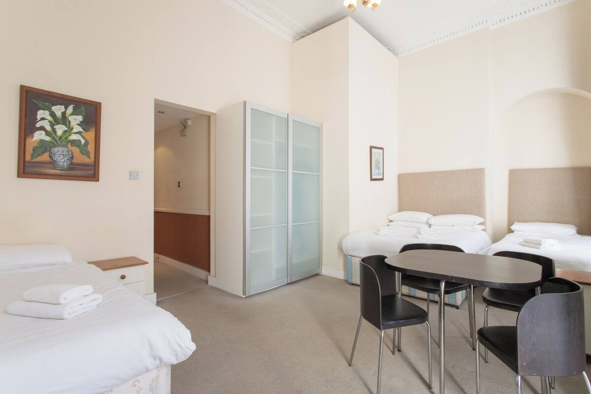 A hotel room with two beds, a dining table with chairs, a wardrobe, and a painting on the wall.