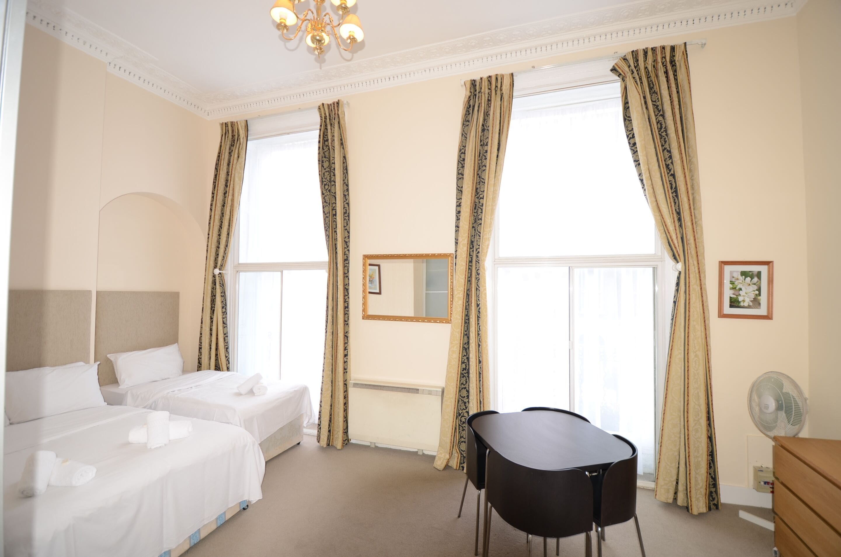Een hotelkamer met twee bedden, een eettafel, een stoel, een spiegel en een ventilator.
