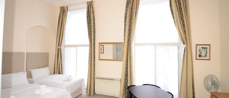 Een hotelkamer met twee bedden, een eettafel, een stoel, een spiegel en een ventilator.