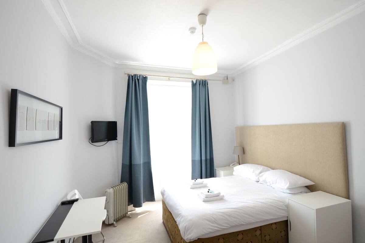 A hotel room with a bed, bedside table, lamp, and a framed picture on the wall.