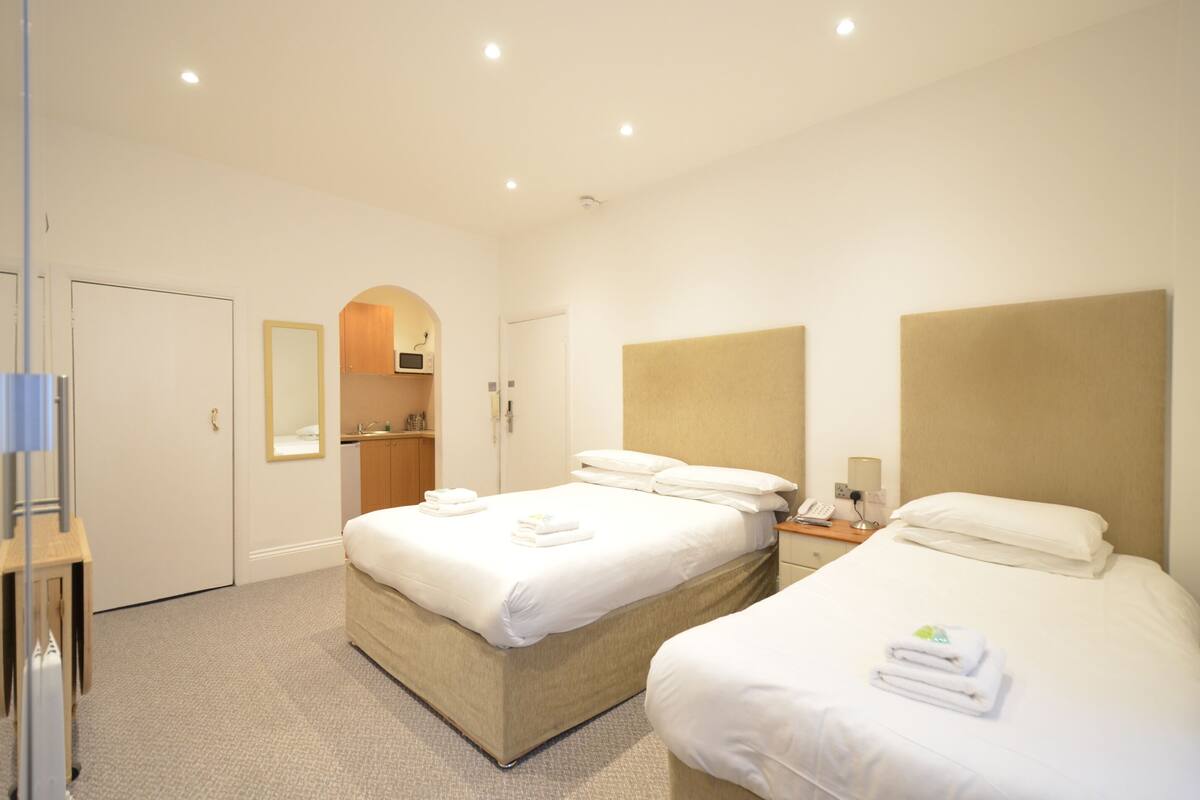 A hotel room with two beds, a bathroom, and a small kitchenette.