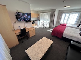 A hotel room with a bed, desk, chair, TV, kitchenette, and a small table.