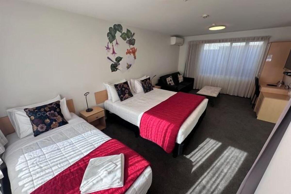 A hotel room with two beds, a desk, and a window with curtains.