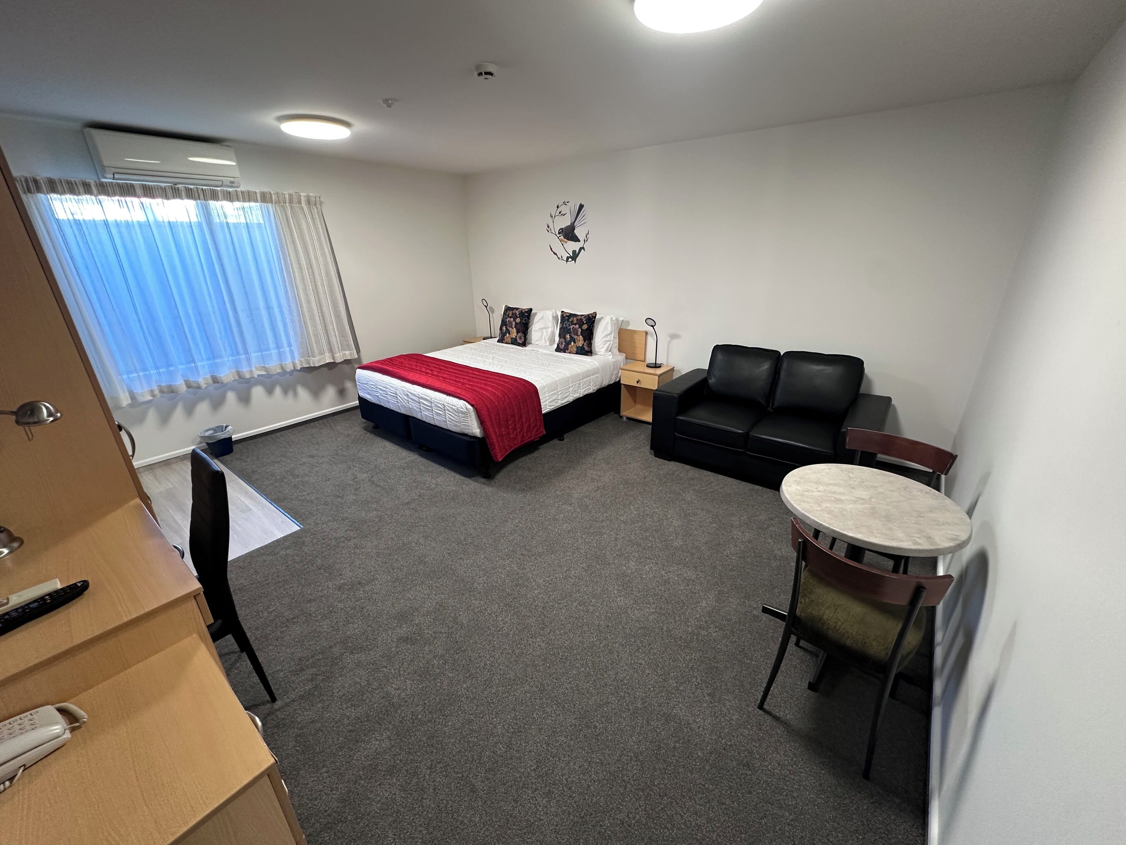 Une chambre d’hôtel avec un lit, un canapé en cuir noir, une petite table ronde, un bureau avec un téléphone et une fenêtre avec des rideaux.