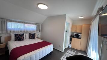 A hotel room with a bed, a small kitchenette, a bathroom, and a view of the city.
