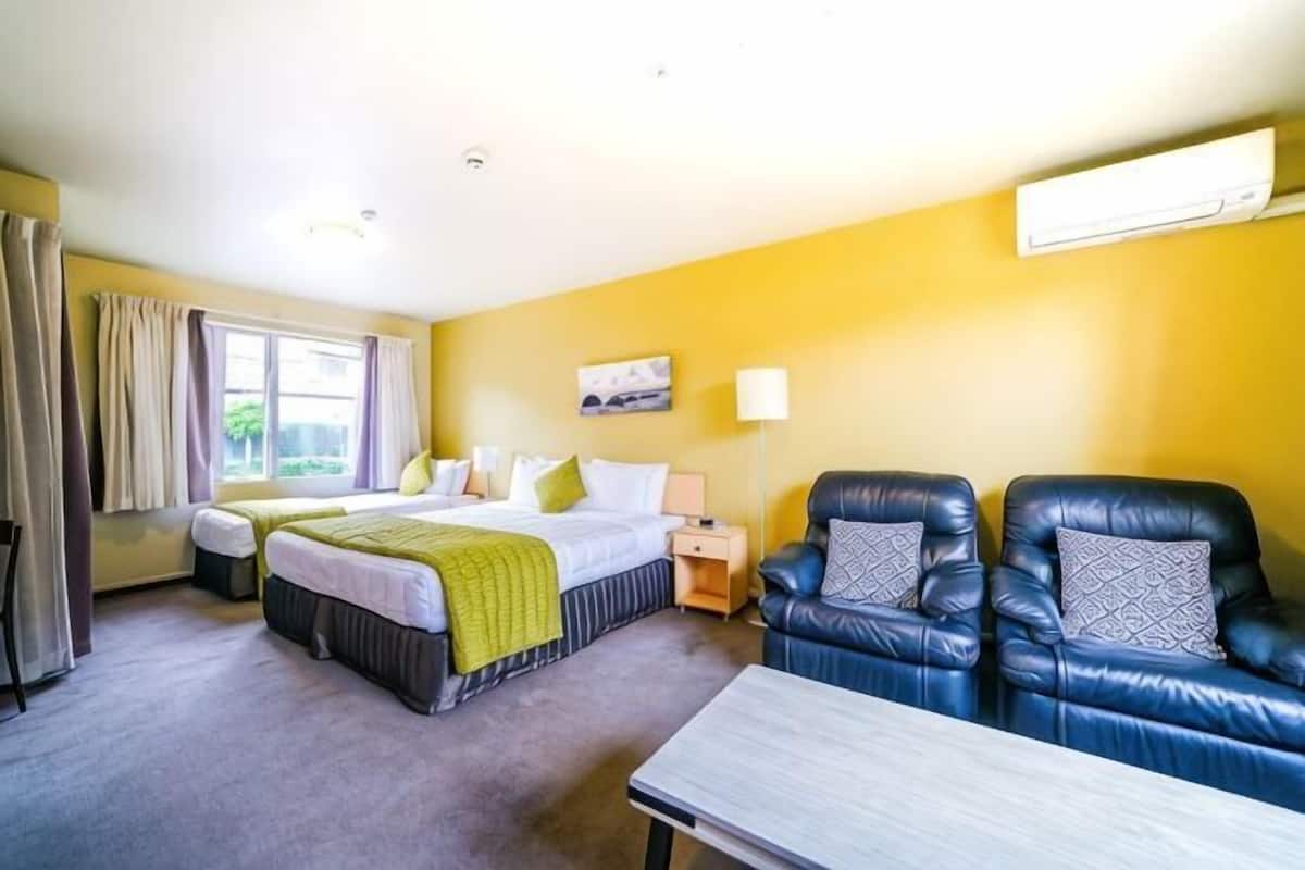 A hotel room with two beds, a sofa, a table, and a window with curtains.