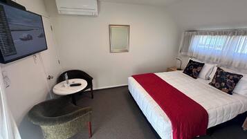 A hotel room with a bed, a chair, a small table, a mirror, and an air conditioning unit.