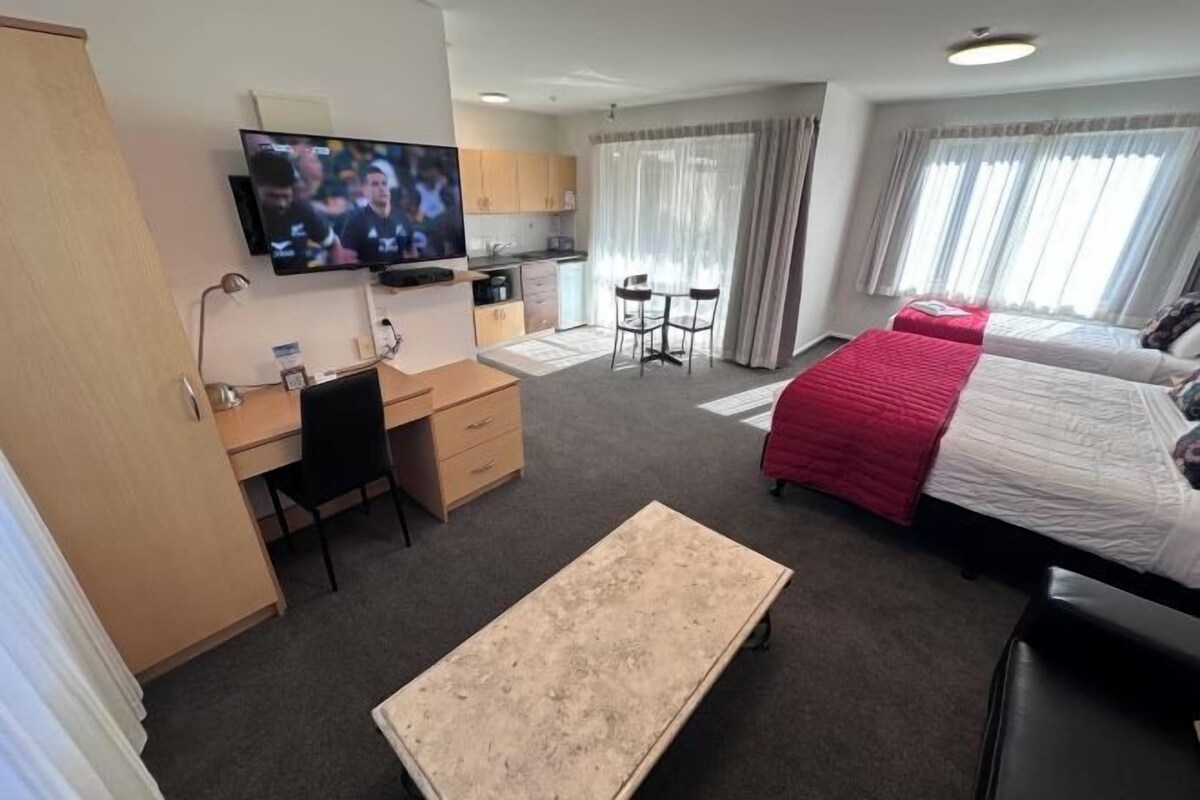 A hotel room with a bed, a desk, a TV, a small kitchen area, and a seating area.