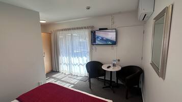 Una habitación de hotel con cama, televisión, dos sillas, una mesita y una ventana con cortinas.