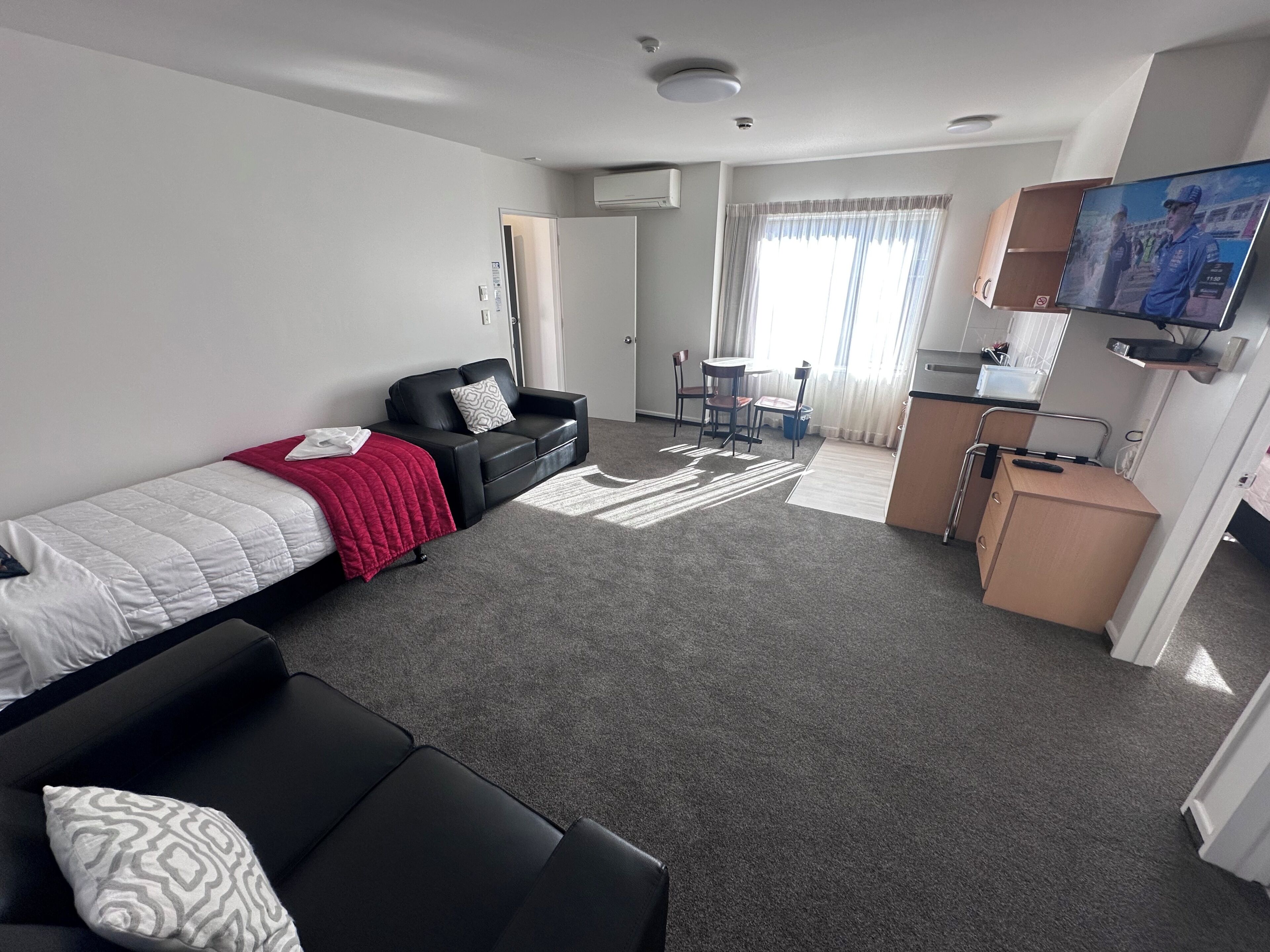 Een kleine hotelkamer met een bed, een slaapbank, een kitchenette en een televisie.