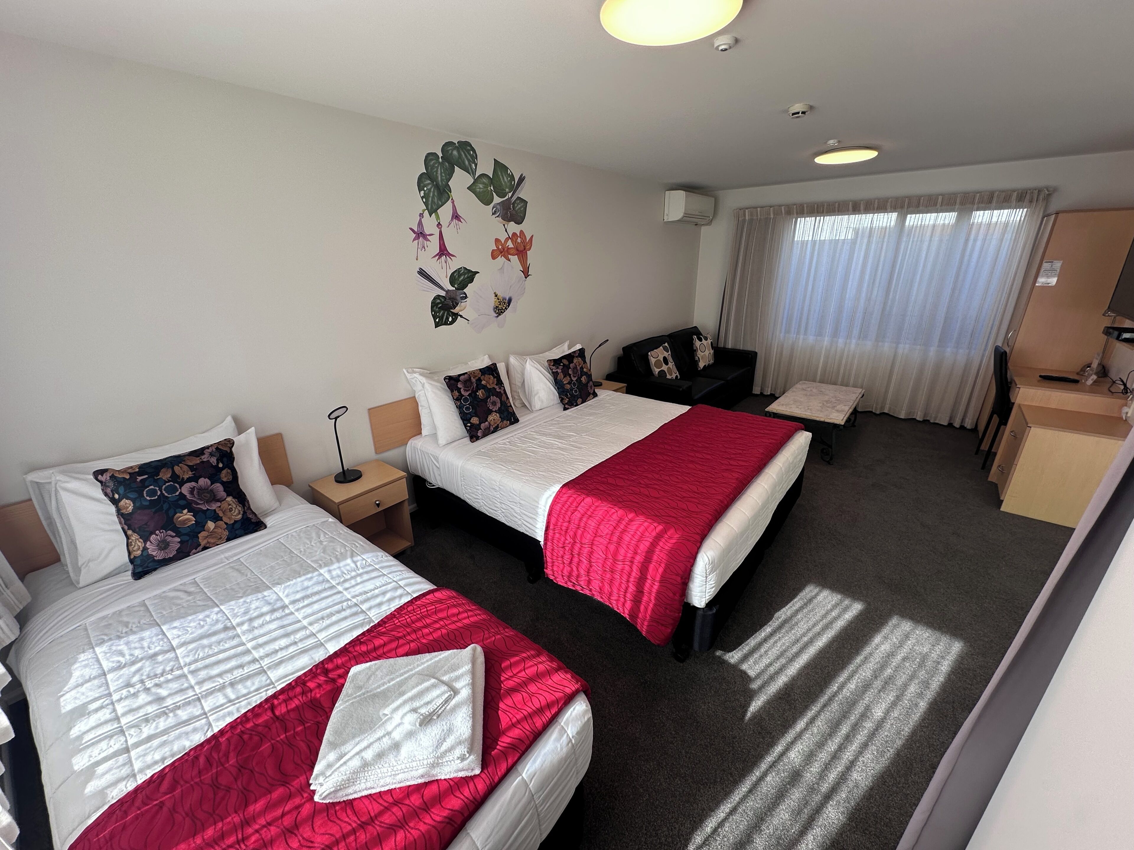 A hotel room with two beds, a desk, a chair, and a window with curtains.