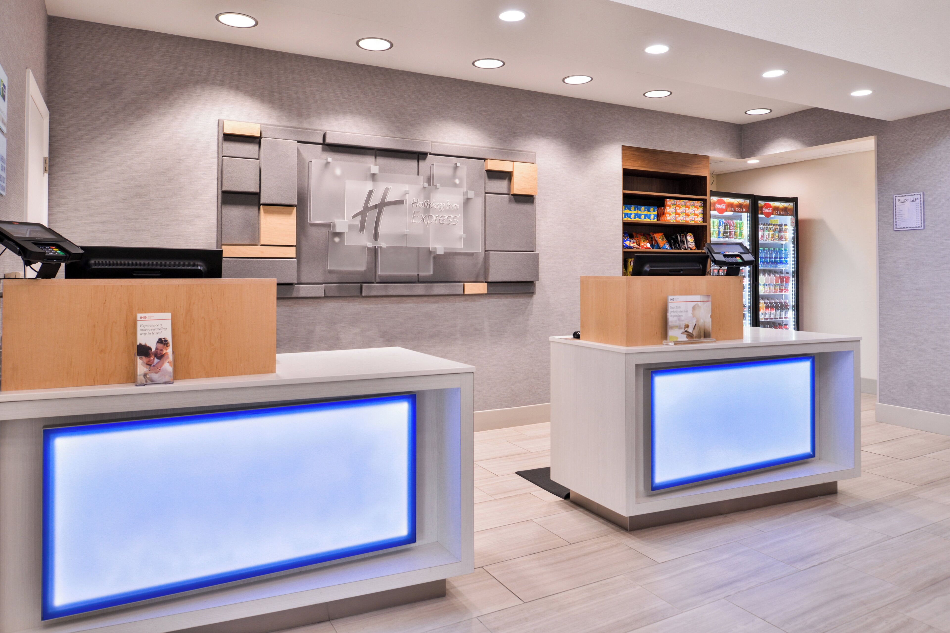 A hotel reception area with two reception desks, a wall-mounted display, vending machines, and a price list on the wall.