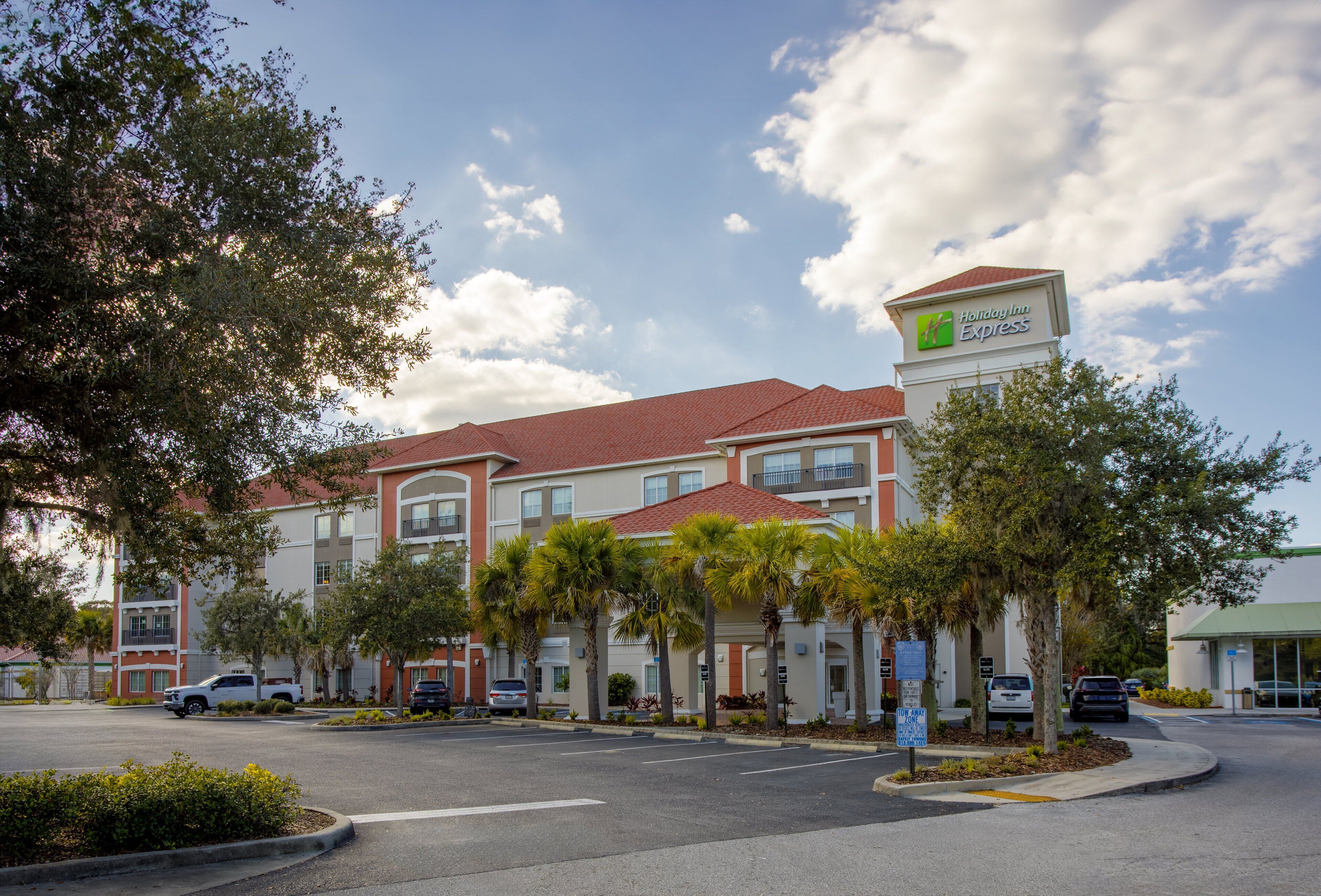 A Holiday Inn Express hotel with a red roof, multiple floors, and a parking lot with several cars.