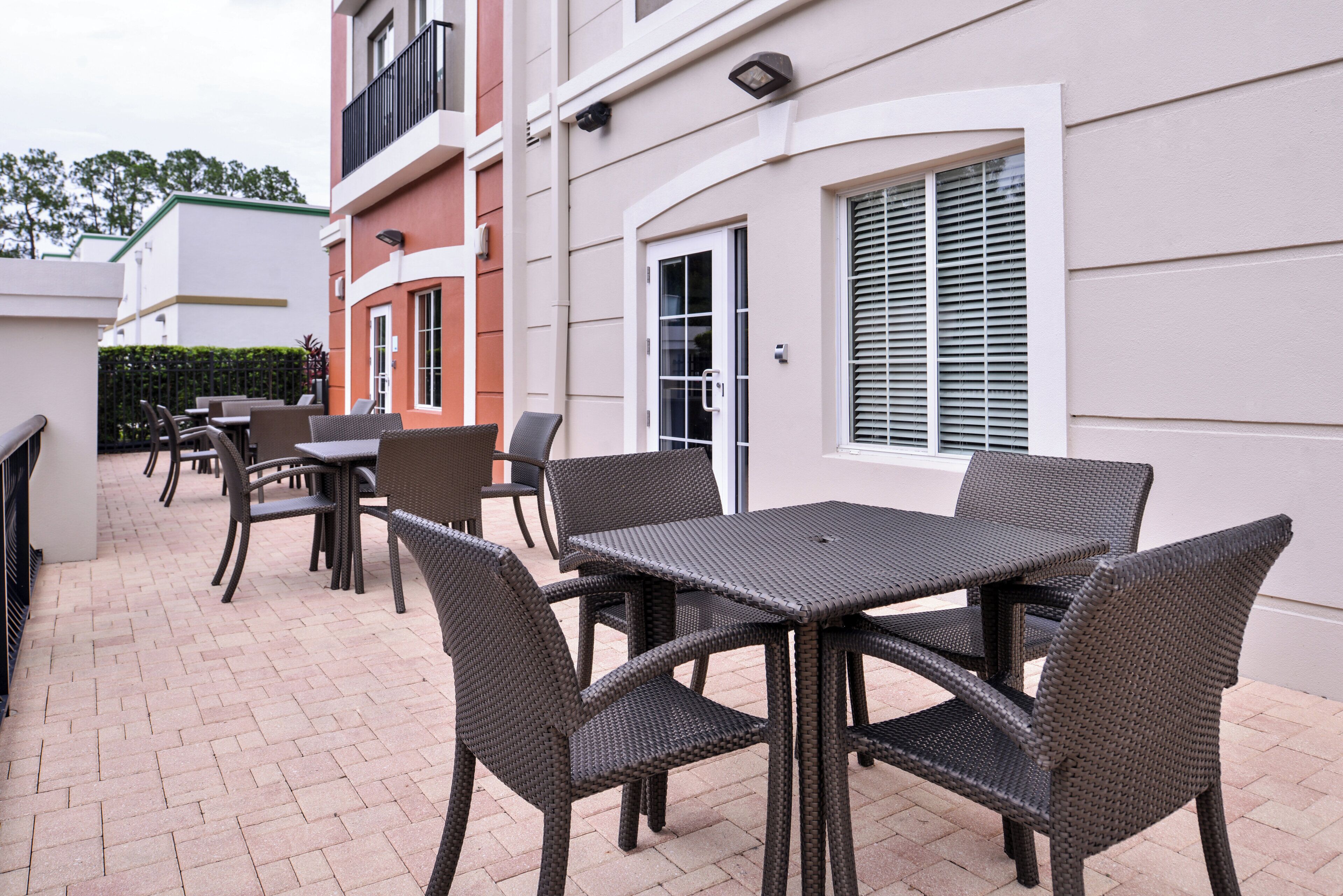 An outdoor patio area with wicker furniture, including tables and chairs, and a brick floor.