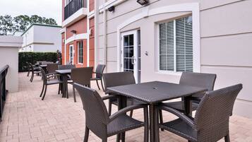 Ein Terrassenbereich im Freien mit Korbmöbeln, darunter Tische und Stühle, und einem Boden aus Ziegelsteinen.
