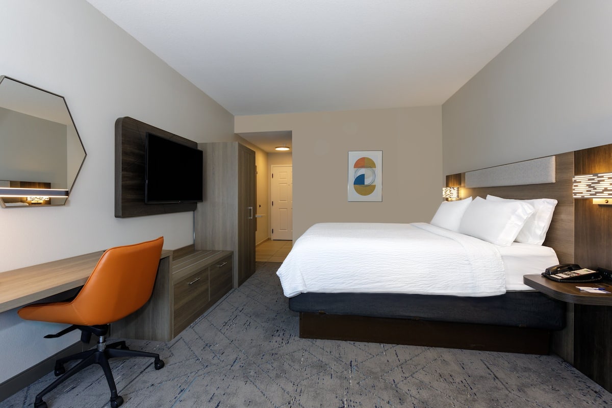 Habitación de hotel con cama, escritorio, silla, televisión y obras de arte.