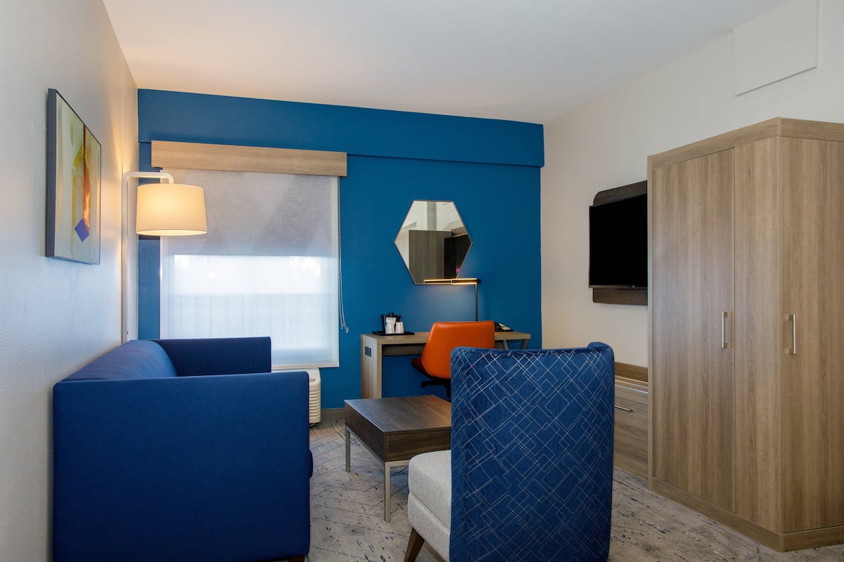 Una habitación de hotel con una pared azul de acento, un armario de madera, un escritorio con una silla y una cama.