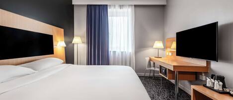 Habitación de hotel con una cama grande, un escritorio, un televisor y una ventana con cortinas.