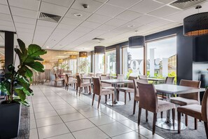 Un espace repas moderne, doté de tables et de chaises, de grandes fenêtres et de plantes d’intérieur.
