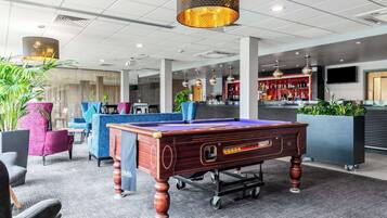 A modern lounge area with a pool table, comfortable seating, and a bar area.