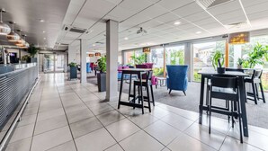 A modern indoor space with a long reception area, multiple seating arrangements, and large windows allowing natural light.