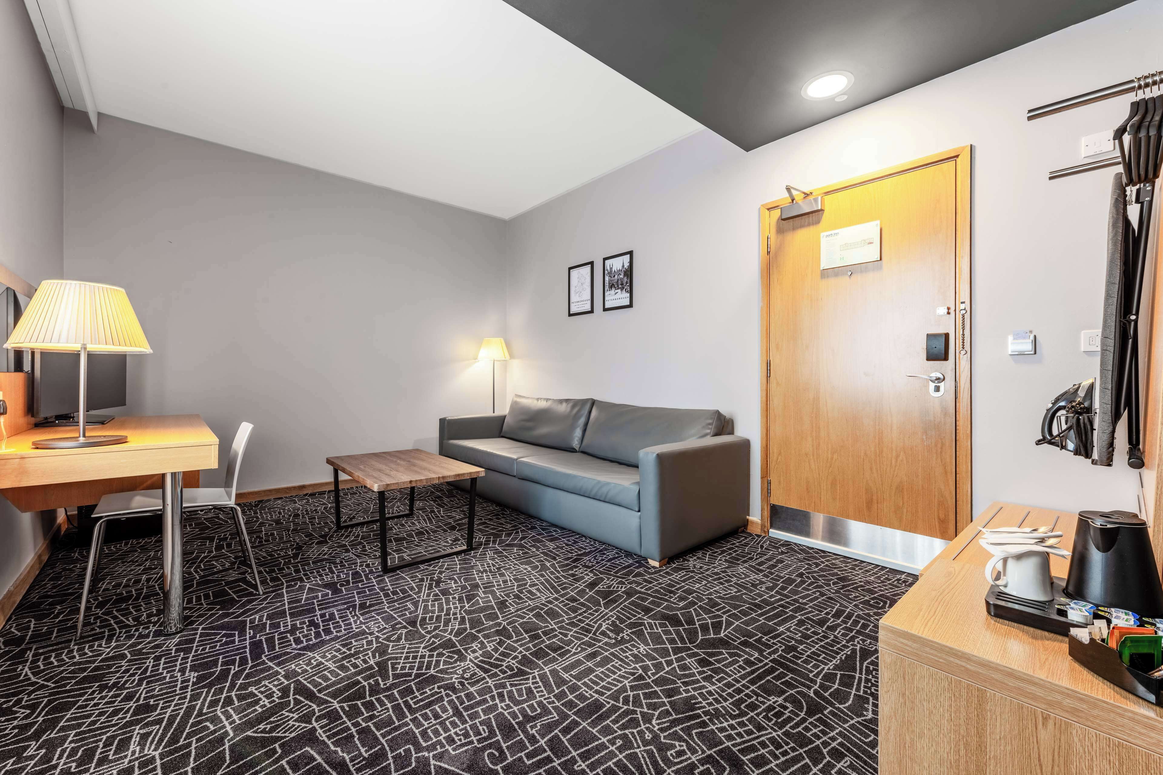 Une chambre d’hôtel équipée d’un bureau, d’un canapé, d’une petite table, d’une lampe, d’un porte-manteau et d’une porte avec une pancarte.