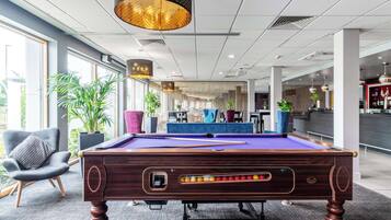 Una mesa de billar en un espacio interior moderno, con una zona de bar al fondo.