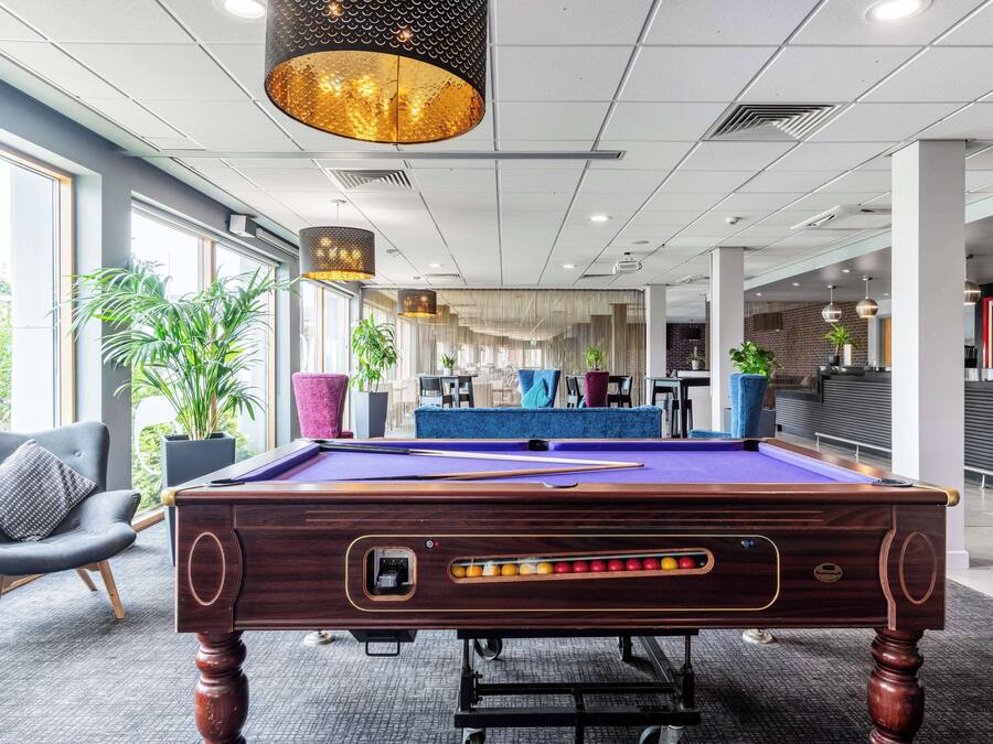 A pool table in a modern indoor setting with a bar area in the background.